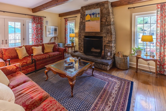 living area with visible vents, wood finished floors, beamed ceiling, baseboards, and a stone fireplace