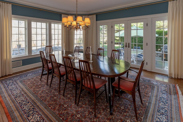 dining space featuring wood-type flooring, french doors, ornamental molding, and a notable chandelier