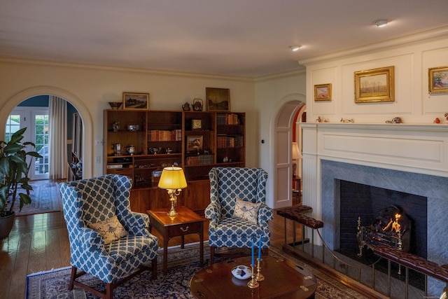 living area with arched walkways, ornamental molding, a lit fireplace, and hardwood / wood-style floors