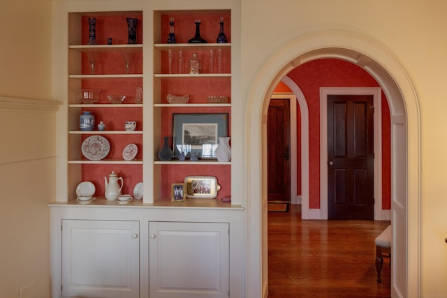 corridor with built in features, arched walkways, and wood finished floors