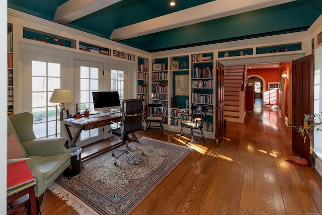 office space featuring arched walkways, built in features, beam ceiling, and hardwood / wood-style floors