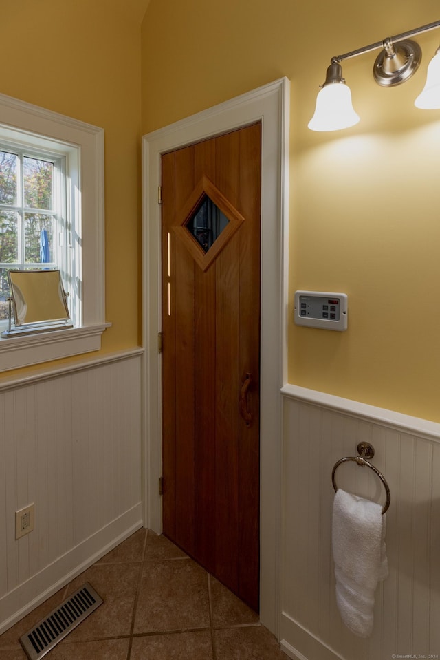 doorway featuring wooden walls, a wainscoted wall, tile patterned floors, and visible vents