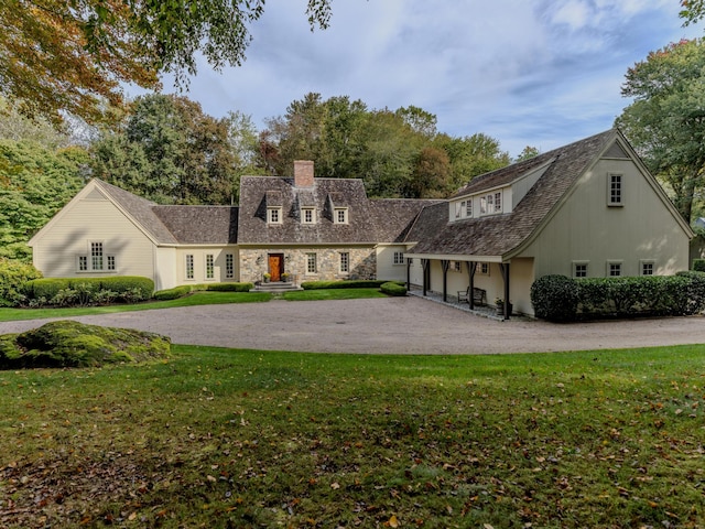 new england style home with curved driveway, a front yard, and a chimney
