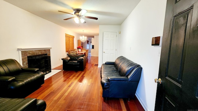 living room with hardwood / wood-style floors, ceiling fan with notable chandelier, and a tiled fireplace