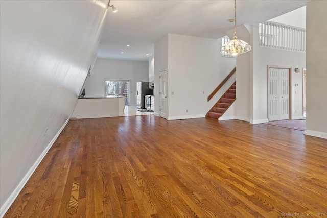 unfurnished living room with wood-type flooring, a high ceiling, and a notable chandelier