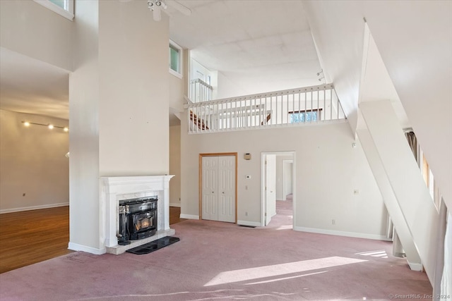 unfurnished living room with ceiling fan, a high ceiling, a high end fireplace, and carpet