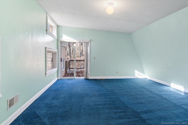 empty room with a wealth of natural light, dark colored carpet, and vaulted ceiling