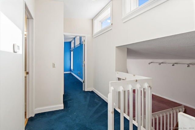 corridor featuring dark colored carpet and a textured ceiling