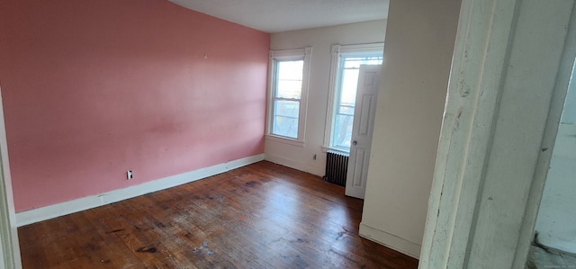 unfurnished room featuring dark wood-type flooring, radiator heating unit, and a healthy amount of sunlight