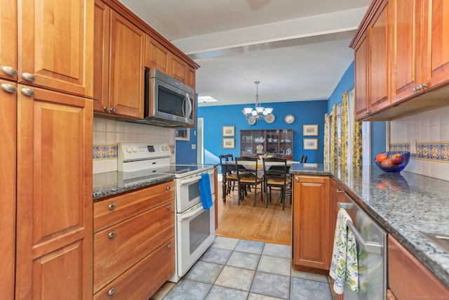 kitchen with tasteful backsplash, pendant lighting, an inviting chandelier, dark stone countertops, and white stove