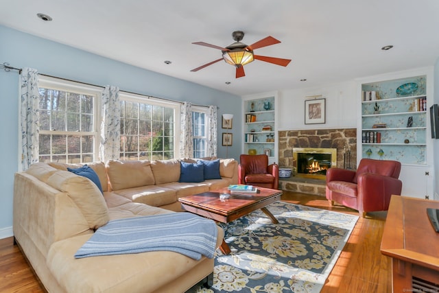 living room with ceiling fan, built in features, a fireplace, and light hardwood / wood-style flooring