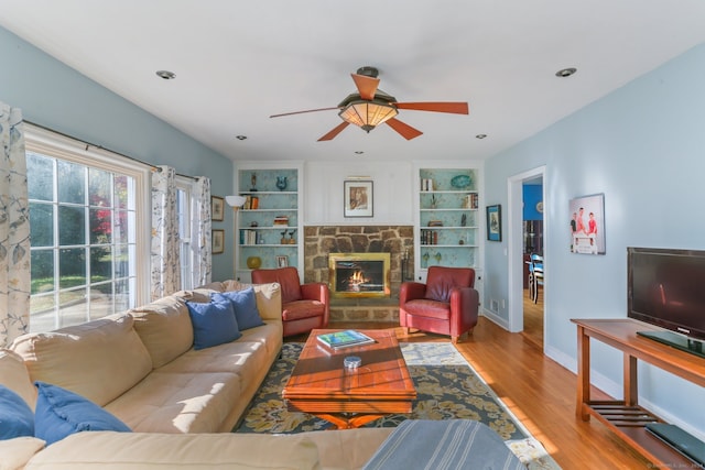 living room featuring built in shelves, ceiling fan, a fireplace, and light wood-type flooring