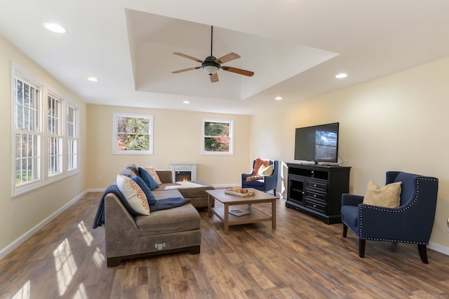 living room with dark hardwood / wood-style flooring, a tray ceiling, and ceiling fan