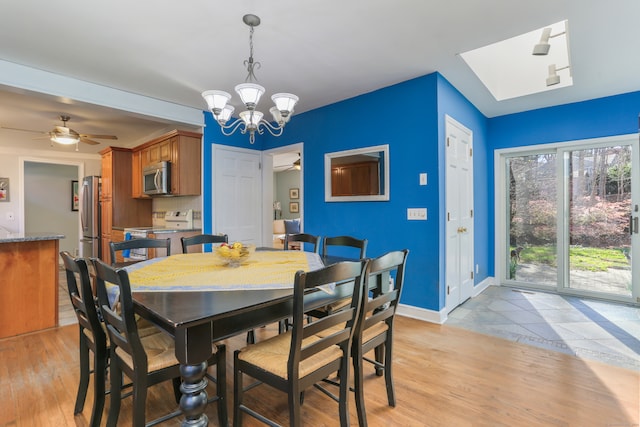 dining space featuring ceiling fan with notable chandelier, a skylight, and light hardwood / wood-style flooring