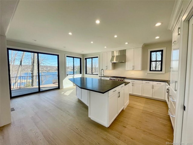 kitchen featuring wall chimney range hood, a healthy amount of sunlight, and white cabinetry