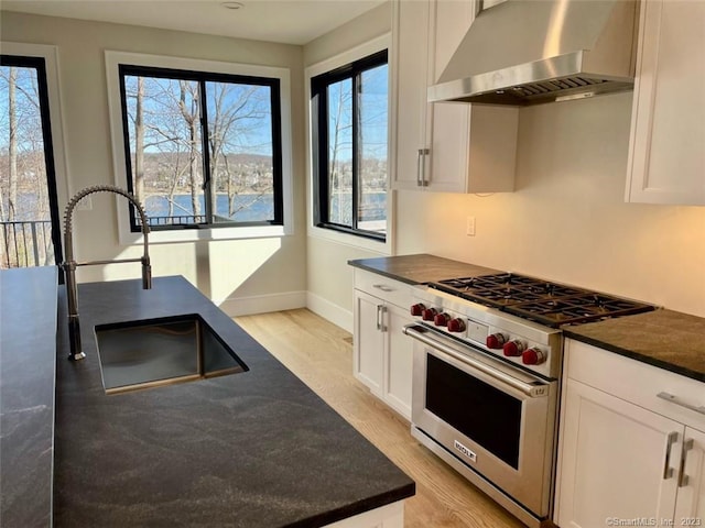 kitchen featuring premium range, sink, wall chimney exhaust hood, and white cabinets