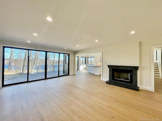 unfurnished living room featuring a high end fireplace, plenty of natural light, and light wood-type flooring