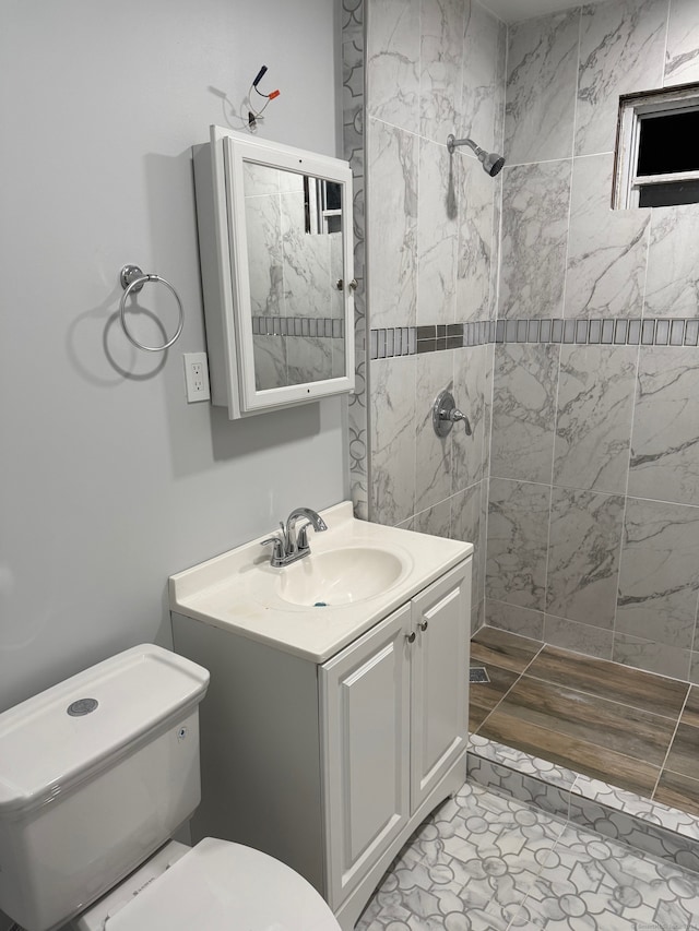 bathroom featuring toilet, hardwood / wood-style floors, vanity, and a tile shower