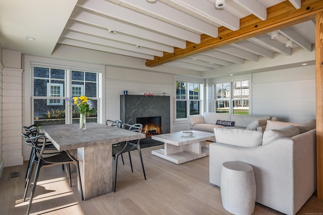 living room featuring a high end fireplace, wooden walls, light wood-type flooring, and beamed ceiling