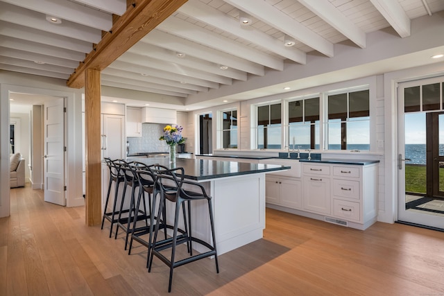 kitchen with white cabinets, light hardwood / wood-style floors, a kitchen island, and beamed ceiling