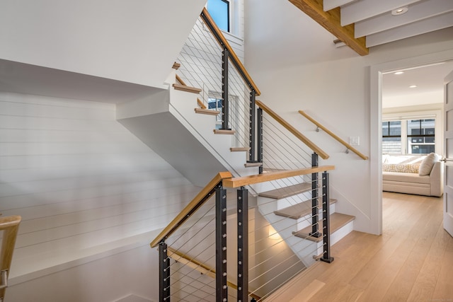 staircase with wood-type flooring and beam ceiling