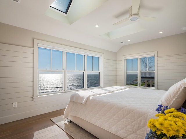 bedroom featuring lofted ceiling with skylight, hardwood / wood-style floors, ceiling fan, and a water view