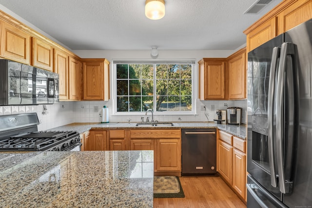 kitchen featuring stainless steel appliances, light hardwood / wood-style floors, sink, light stone counters, and tasteful backsplash