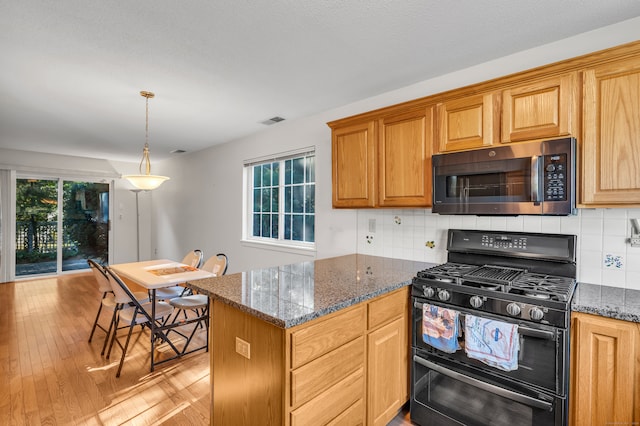 kitchen featuring black range with gas stovetop, dark stone counters, light hardwood / wood-style floors, and tasteful backsplash