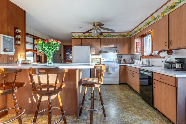 kitchen featuring ceiling fan, sink, kitchen peninsula, white appliances, and a breakfast bar area