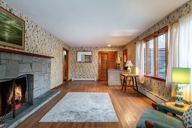 living room featuring hardwood / wood-style flooring, a baseboard radiator, and a stone fireplace