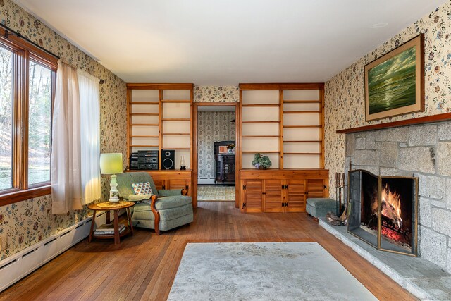 living room with baseboard heating, a fireplace, a healthy amount of sunlight, and hardwood / wood-style flooring