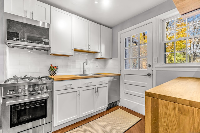 kitchen with stainless steel appliances, white cabinetry, butcher block counters, and sink