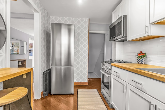 kitchen with appliances with stainless steel finishes, backsplash, wood-type flooring, butcher block countertops, and white cabinetry