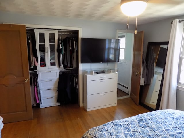 bedroom with hardwood / wood-style floors, a baseboard radiator, and a closet