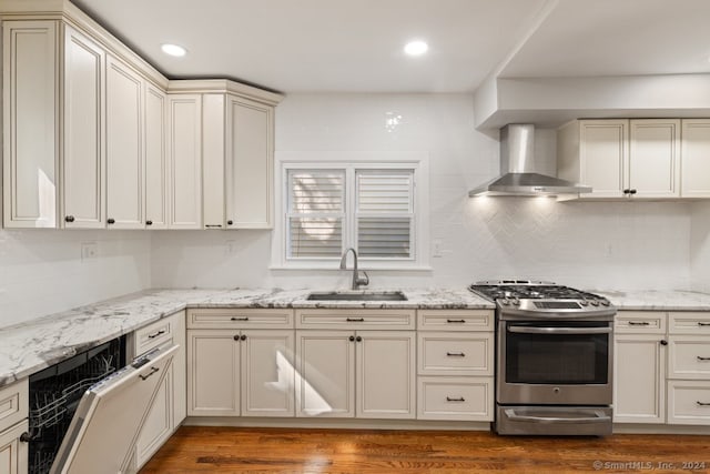 kitchen featuring hardwood / wood-style floors, cream cabinets, wall chimney range hood, sink, and gas stove