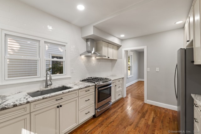 kitchen featuring sink, wall chimney exhaust hood, light stone counters, dark hardwood / wood-style flooring, and stainless steel appliances