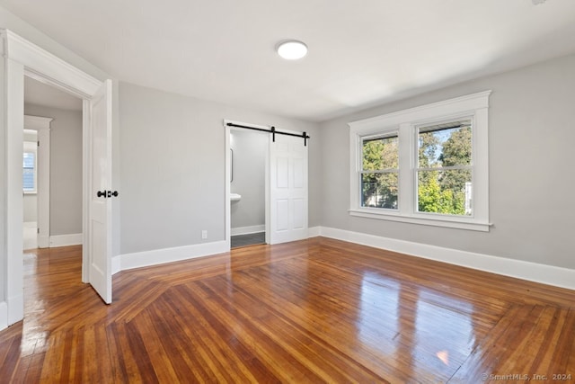 unfurnished bedroom featuring a barn door, hardwood / wood-style floors, and ensuite bath