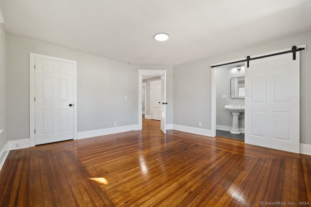 unfurnished bedroom featuring a barn door, ensuite bathroom, sink, and hardwood / wood-style flooring