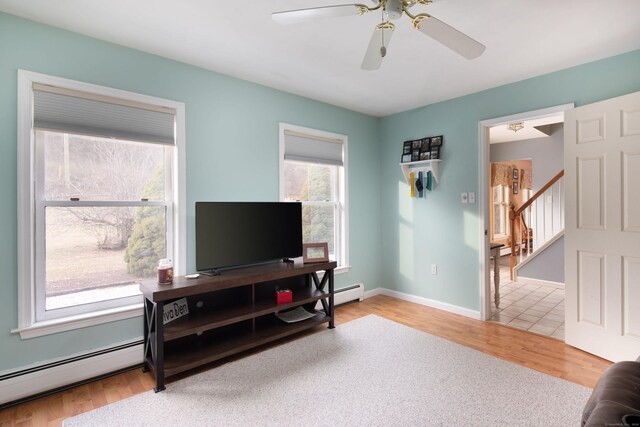 living room featuring ceiling fan, a healthy amount of sunlight, wood-type flooring, and a baseboard heating unit