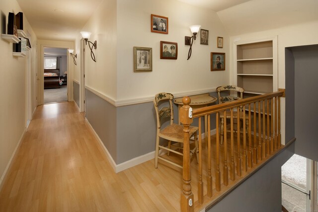 corridor with built in shelves, light hardwood / wood-style floors, and lofted ceiling