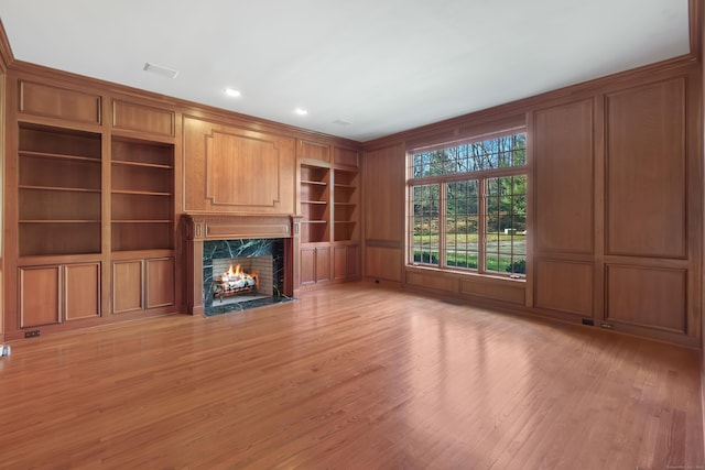 unfurnished living room with a high end fireplace, light wood-type flooring, and built in features