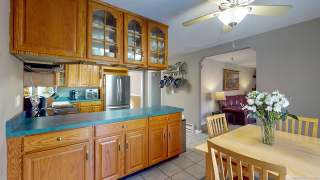 kitchen featuring a textured ceiling, ceiling fan, light tile patterned floors, black range, and stainless steel refrigerator