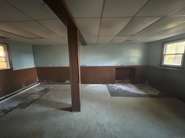 basement featuring a drop ceiling, wood walls, and light carpet