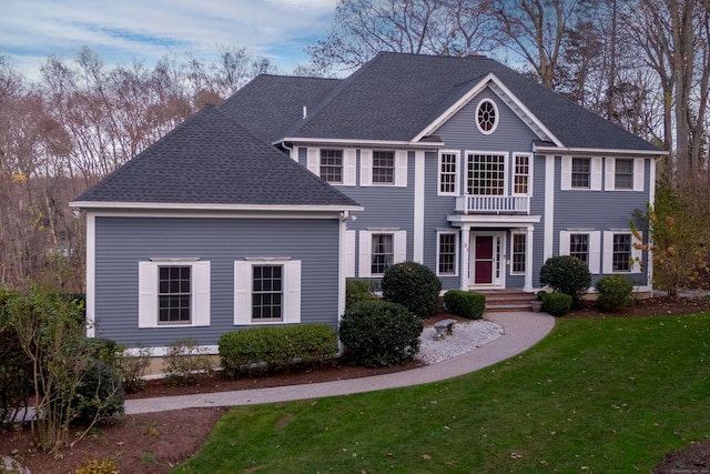 colonial home featuring a balcony and a front yard