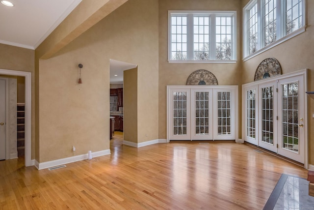 unfurnished living room featuring a towering ceiling, light hardwood / wood-style floors, and crown molding