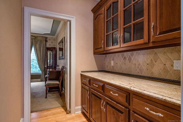 bar with tasteful backsplash, light stone countertops, crown molding, and light wood-type flooring