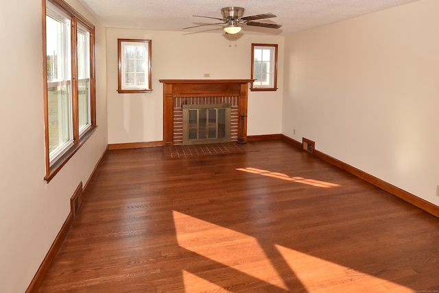 unfurnished living room featuring ceiling fan, dark hardwood / wood-style flooring, a textured ceiling, and a brick fireplace