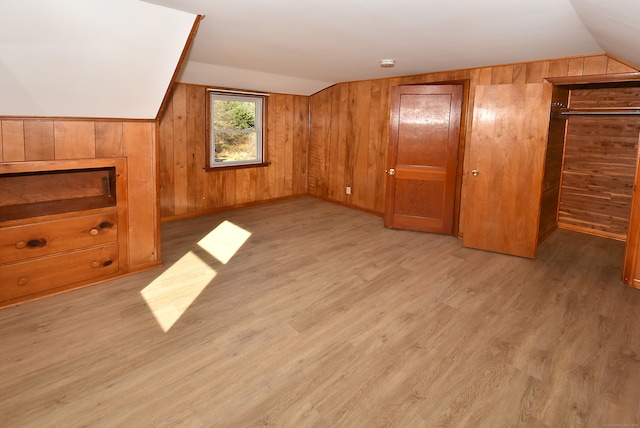 additional living space with wood walls, light wood-type flooring, and vaulted ceiling