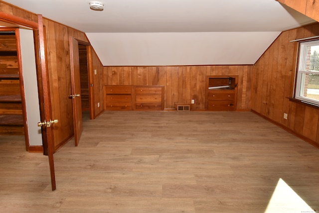 additional living space featuring light wood-type flooring, vaulted ceiling, and wood walls