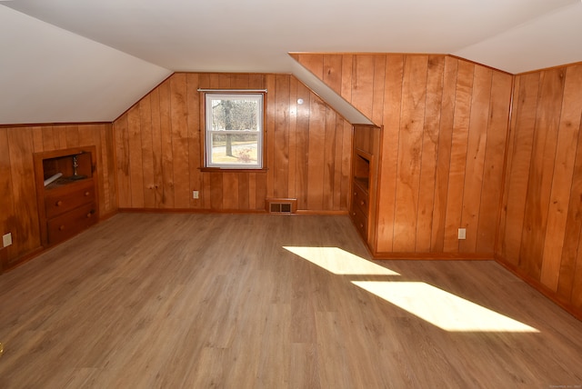 additional living space with wooden walls, light hardwood / wood-style floors, and vaulted ceiling